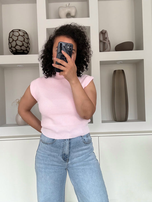 Lichtroze gebreide mouwloze top met hoge hals en ribstructuur, aangesloten model, gedragen op een blauwe high waist jeans