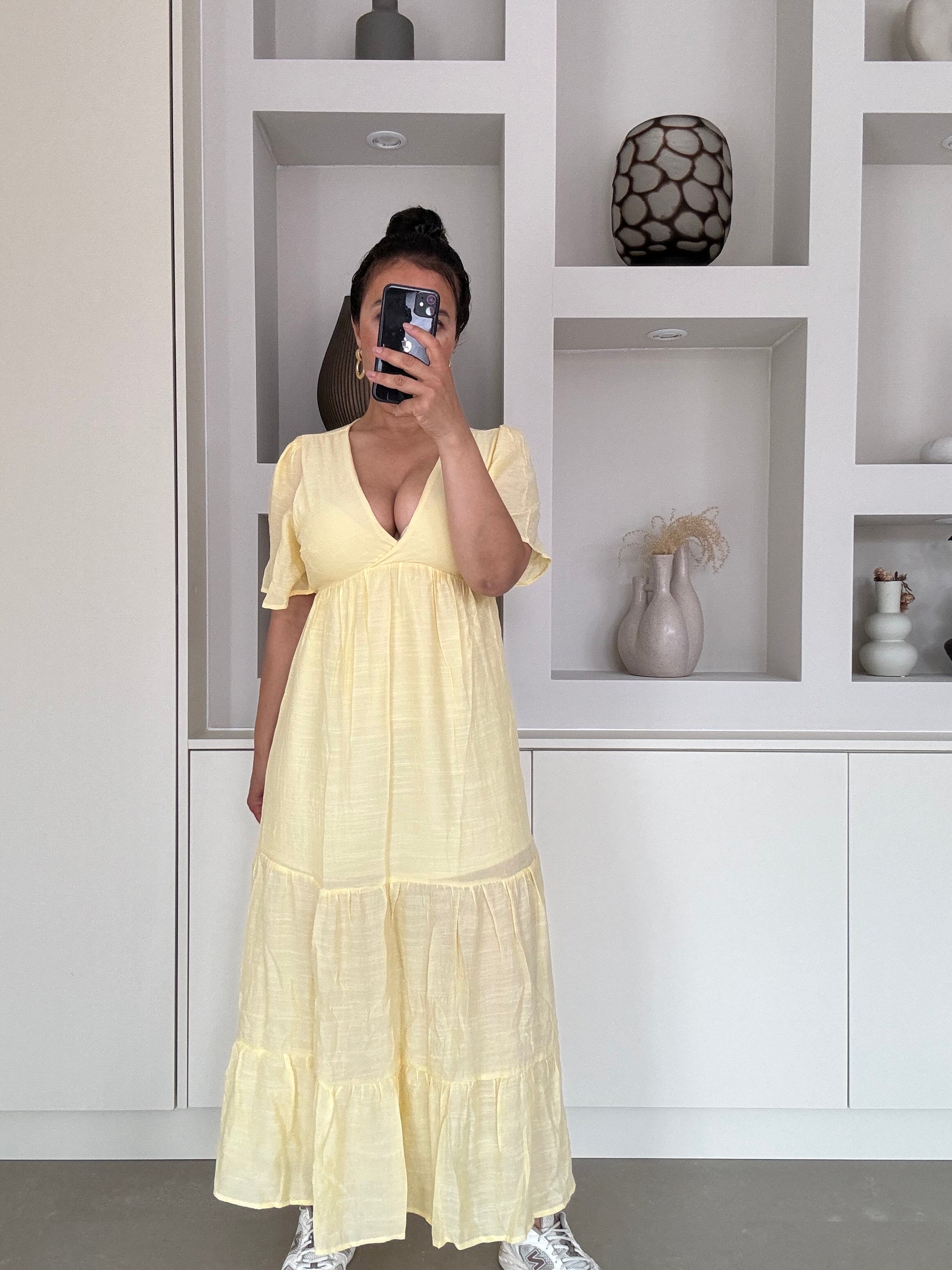 Model draagt een luchtige maxi-jurk met diepe V-hals en korte vlindermouwen in lichtgele kleur, perfect voor warme zomerdagen