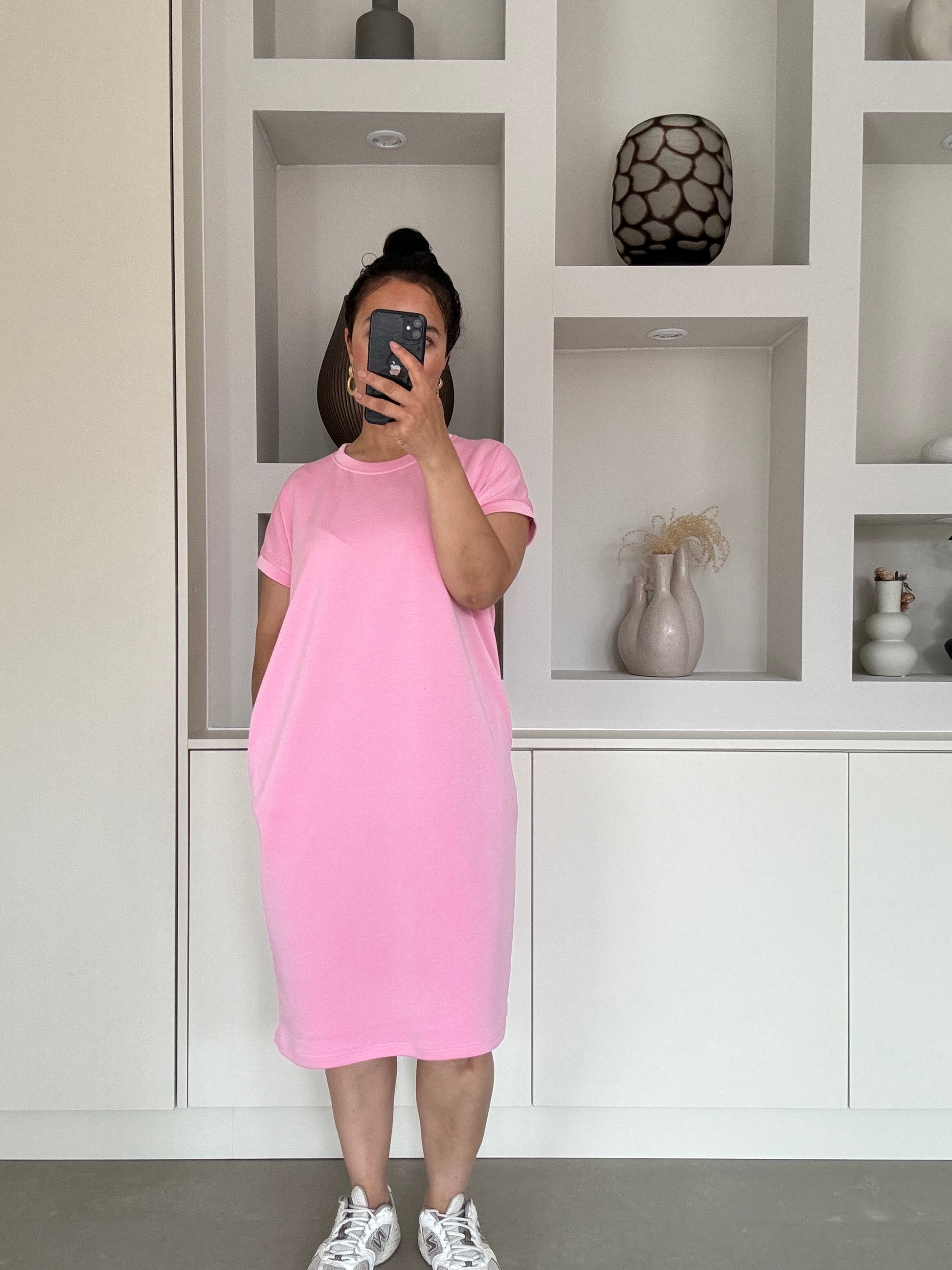 Model draagt een lichtroze, casual T-shirtjurk met korte mouwen en relaxte pasvorm, gemaakt van een zachte katoenmix.