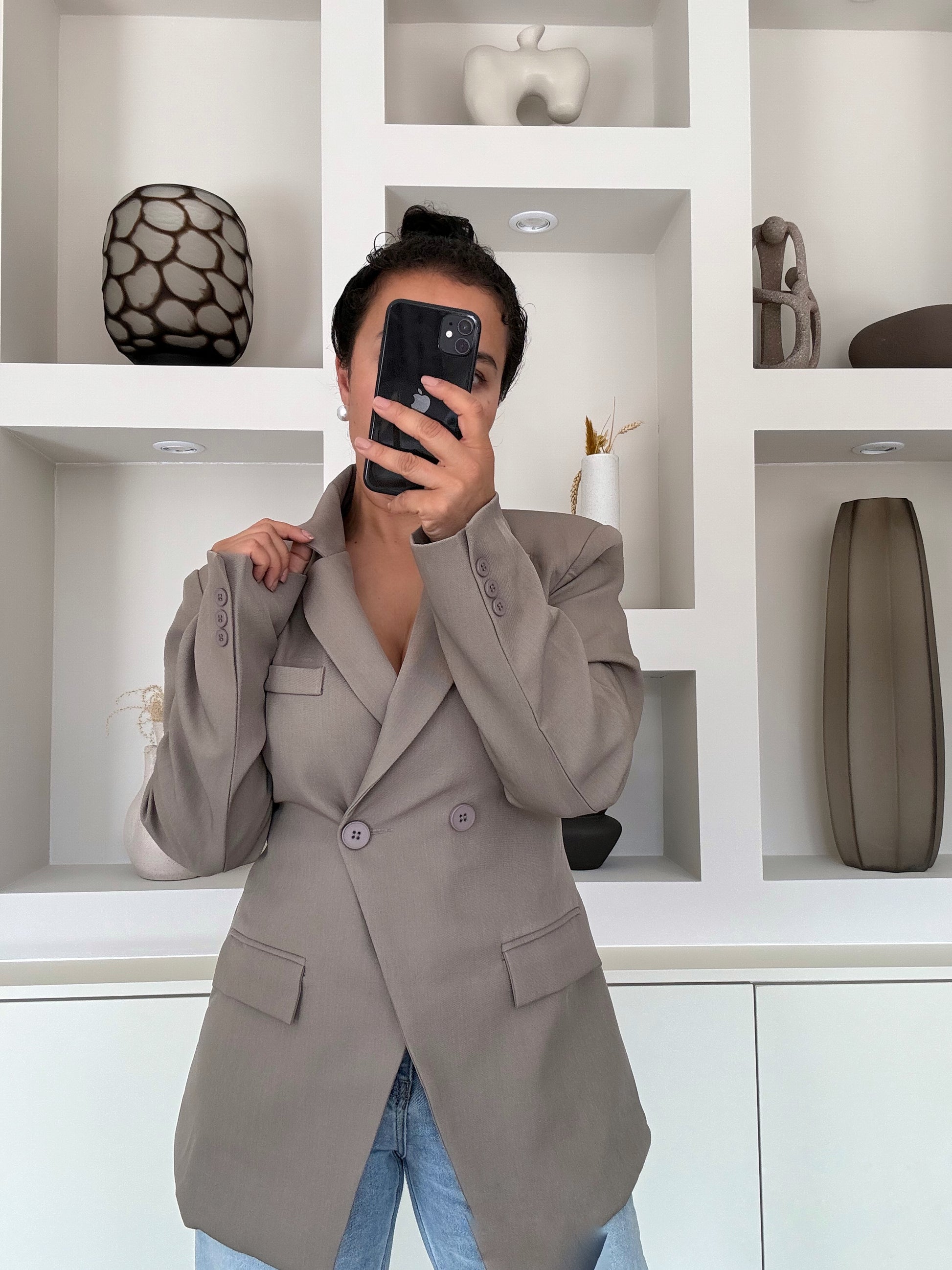Model draagt een taupekleurige blazer met een dubbele knoopsluiting, gestructureerde schouders en een getailleerde pasvorm, gestyled met een lichte jeans