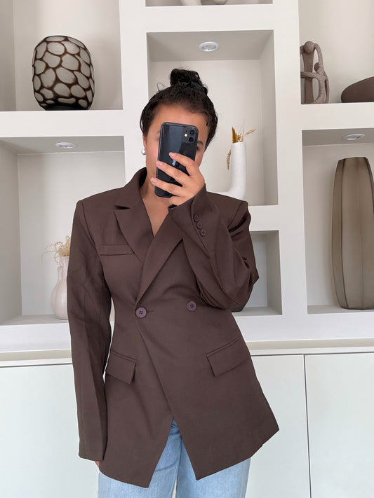 Model draagt een donkerbruine blazer met dubbele knoopsluiting, getailleerde pasvorm en gestructureerde schouders, gecombineerd met een blauwe jeans.