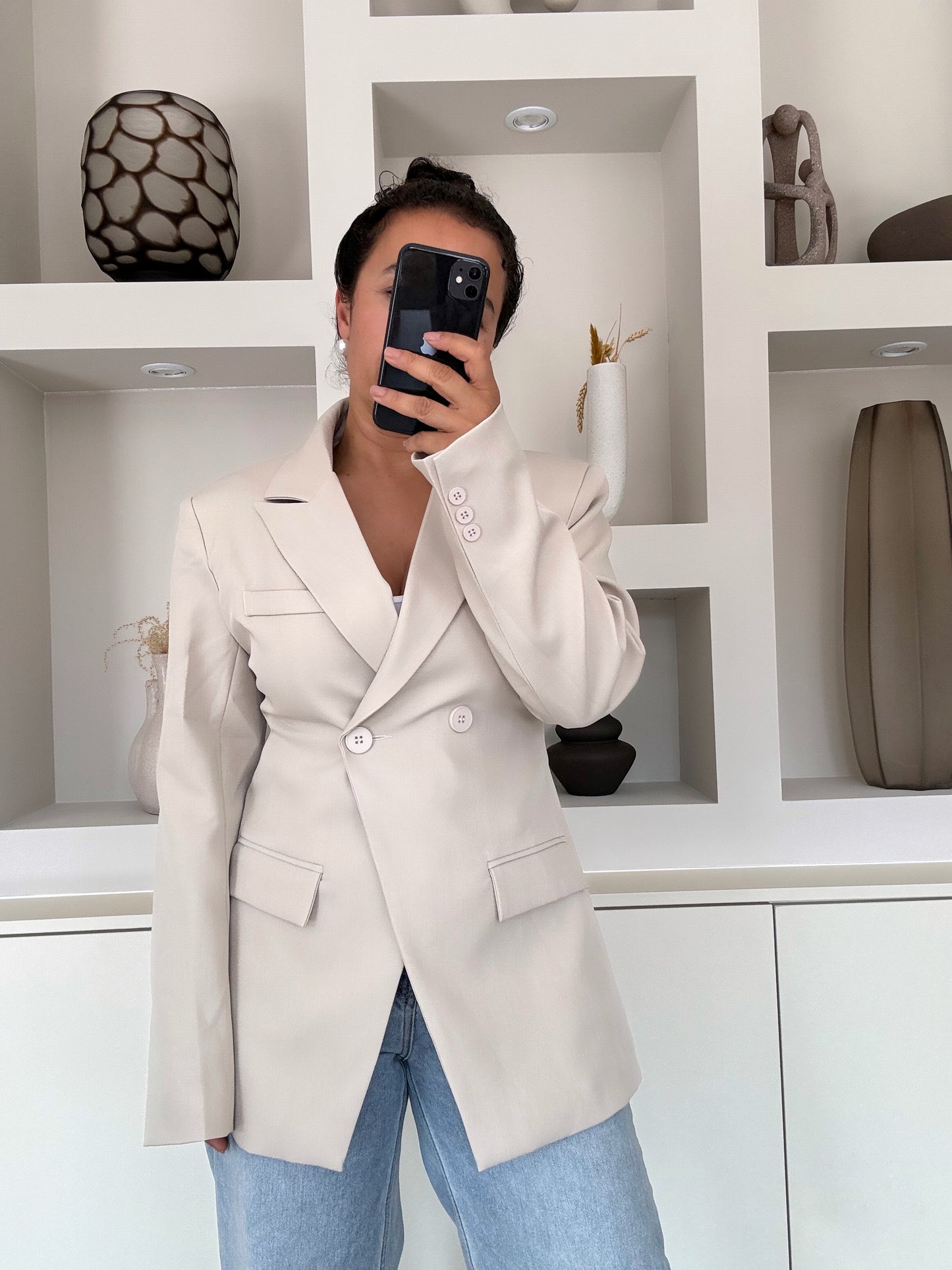 Model draagt een beige blazer met dubbele knoopsluiting, gestructureerde schouders en een vrouwelijke, getailleerde pasvorm, gecombineerd met een lichte jeans.