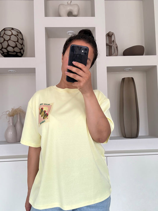 Model draagt The olive girl tee in pastelgele kleur met illustratie en tekst op de borst – VYNAH