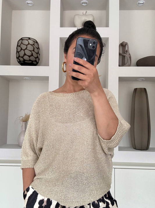Model draagt de Nora shimmer knit met vleermuismouw en metallic glans in goudzand kleur – VYNAH