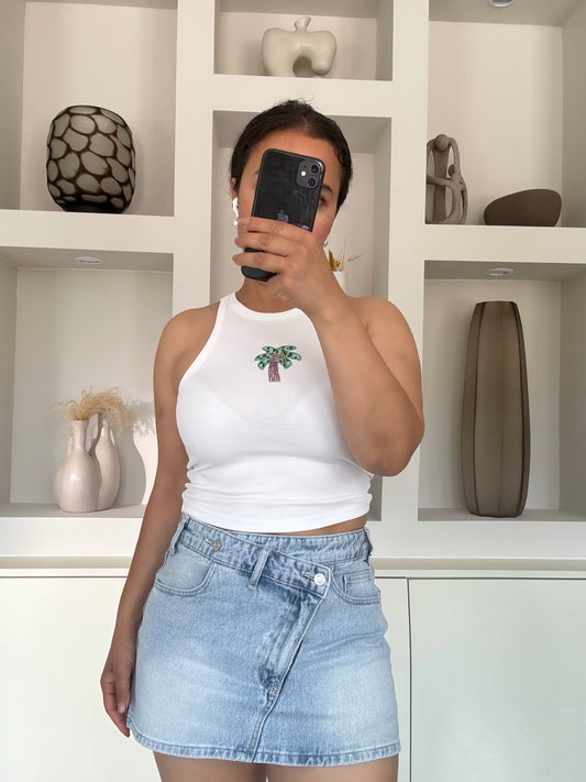 Model draagt witte rib top met palmboom-borduursel van VYNAH