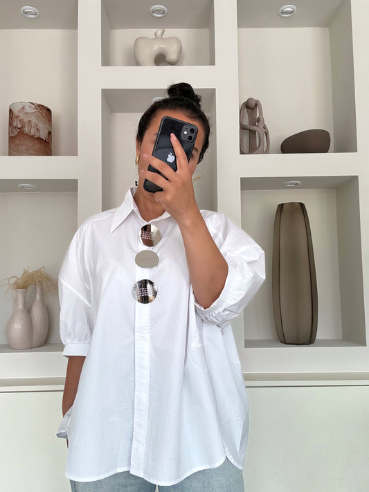 Model draagt witte katoenen oversized blouse van VYNAH met opgerolde mouwen