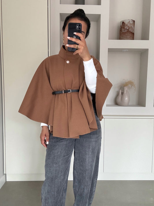 Vrouw met karamelbruine cape met riem en hoge kraag, over witte top en grijze jeans – VYNAH