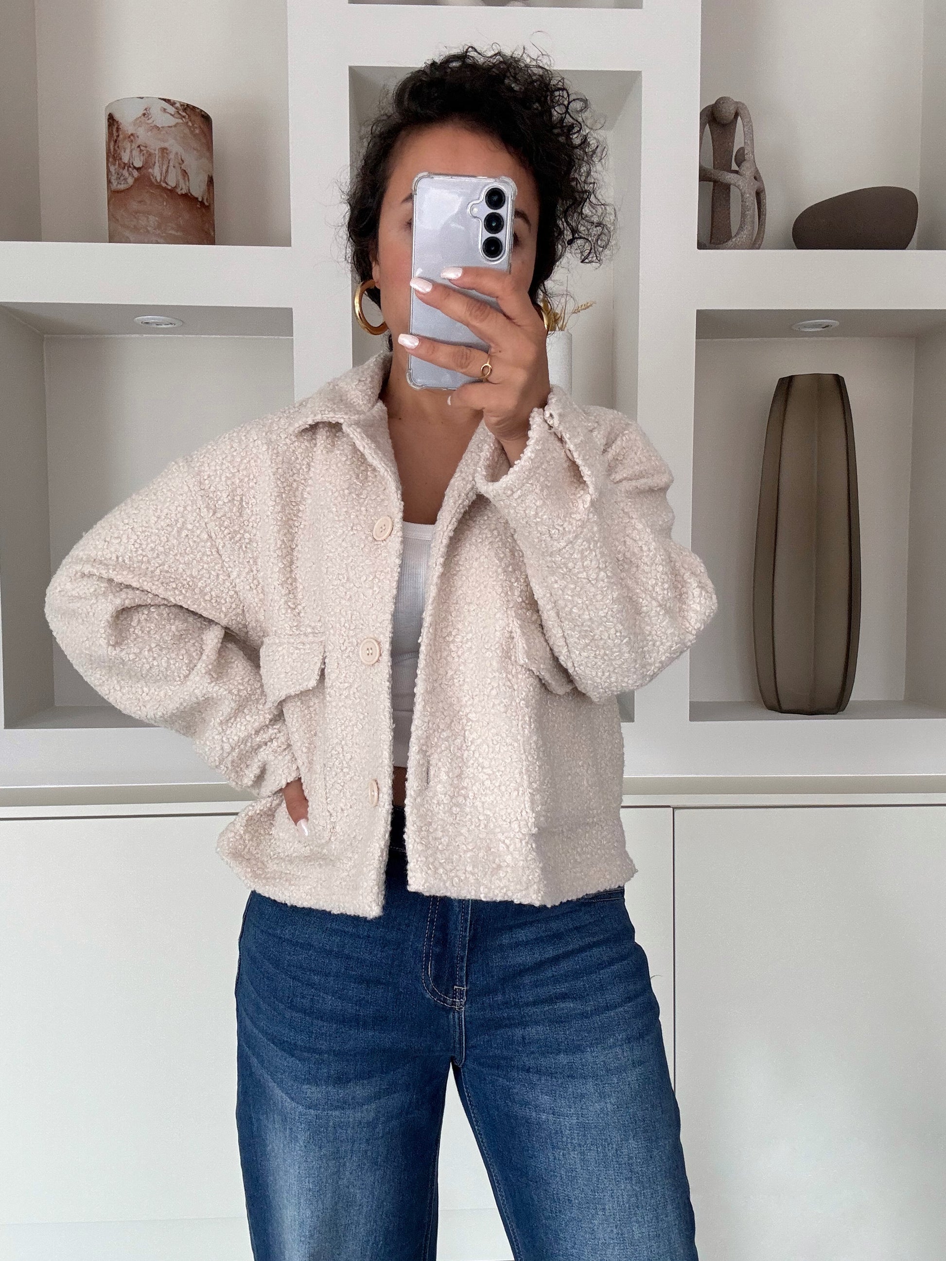 Vrouw met ecru teddy jas met knoopsluiting en klepzakken, gedragen over witte top en jeans – VYNAH